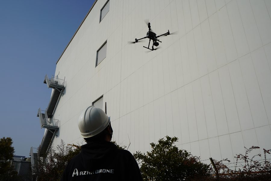 建物の外壁に沿って調査飛行するドローンとパイロット